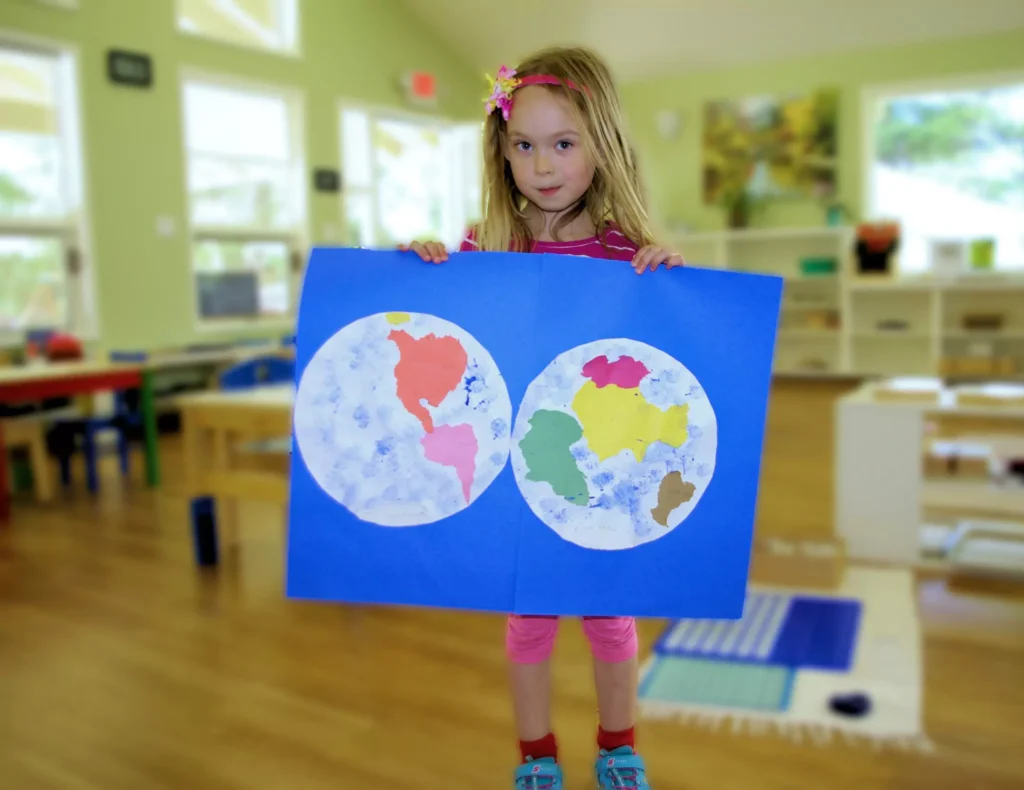 a girl holding a world map drawing in aster montessori school